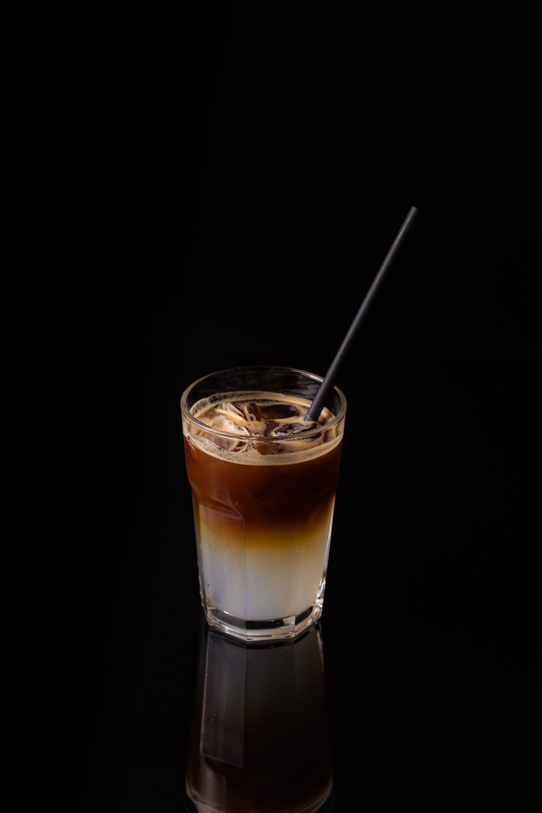 Cafea la gheață, în straturi de lapte și cafea, într-un pahar cu pai negru