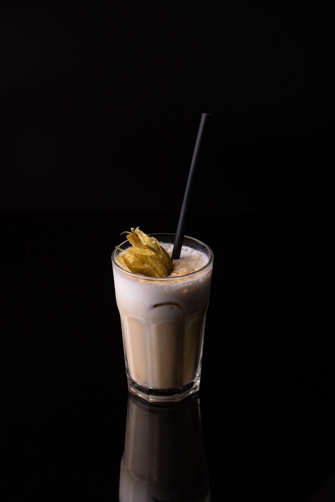 Cafea cu lapte în pahar înalt, cu spumă, physalis și pai negru